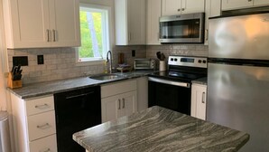 A modern kitchen with white cabinets, a granite countertop, a stainless steel refrigerator, a microwave, and a dishwasher. - Ski On, Ski off Okemo Trailside Appartment, Sleeps 6/ $550per night, (Ludlow)