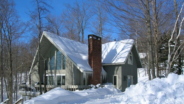 A two-story house with a steeply pitched roof, surrounded by snow-covered ground and trees. - Ski On, Ski off Okemo Trailside Appartment, Sleeps 6/ $550per night, (Ludlow)