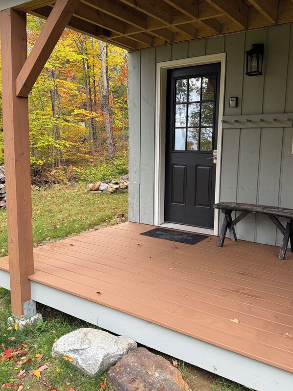 A wooden deck with a black door, a bench, and a stone wall in the background.