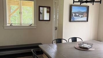 A dining area with a table, chairs, a chandelier, a window with blinds, a mirror, and a framed picture on the wall.