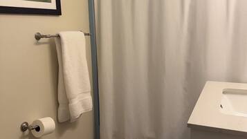 A bathroom with a shower curtain, a toilet, a sink, a framed picture on the wall, and a small rug.
