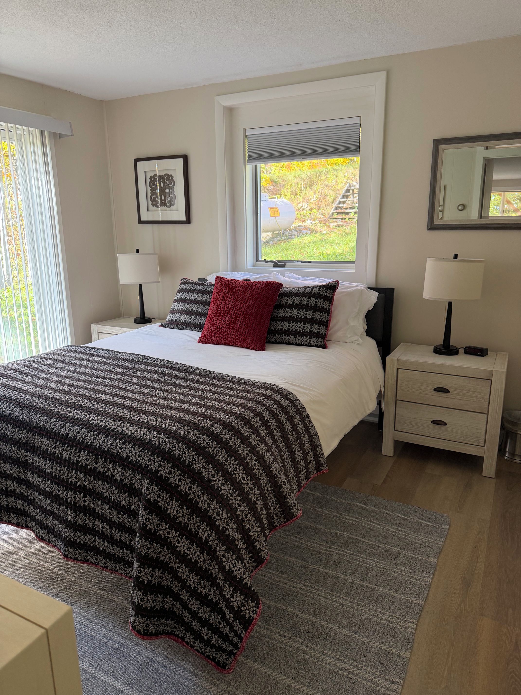 A bedroom with a bed, two bedside tables, a window with a view, and a framed picture on the wall.