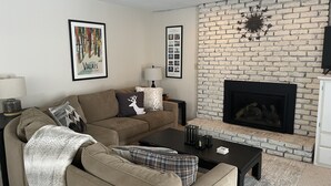 A living room with a sectional sofa, a fireplace, and a wall-mounted TV. - Ski On, Ski off Okemo Trailside Appartment, Sleeps 6/ $550per night, (Ludlow)