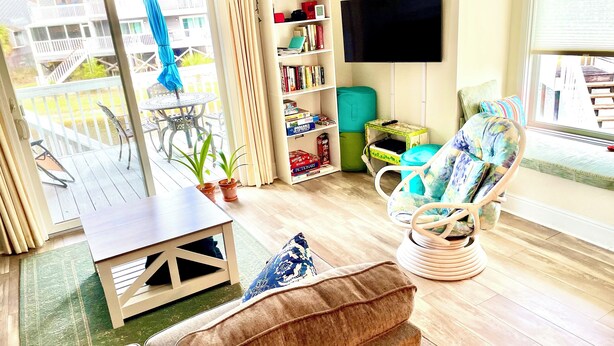 A living room with a sofa, a chair, a table, a bookshelf, a TV, and a balcony with outdoor furniture. - Pet-Friendly Beach Retreat Near Pool/Pickle Ball Courts With Weekly Discounts! (Port St Joe)