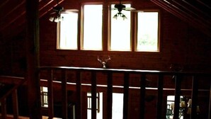 A rustic wooden interior with a high ceiling, a balcony with a railing, and three windows allowing natural light. - Log Cabin-Unique/Beautiful (Candor)