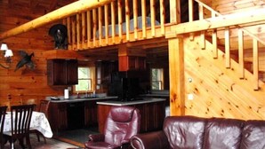 A wooden cabin interior with a dining area, kitchen, and a living room with leather furniture. - Log Cabin-Unique/Beautiful (Candor)