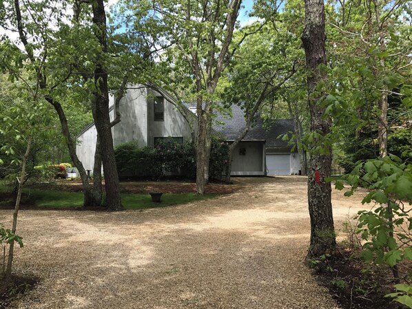 A gravel driveway leading to a white building with a garage, surrounded by trees and shrubs.