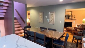 Un espace repas avec une table en marbre, des chaises recouvertes d’un tissu bleu et un escalier en bois.