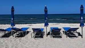 Una playa con cinco tumbonas y sombrillas azules a juego, dispuestas en fila sobre la arena.