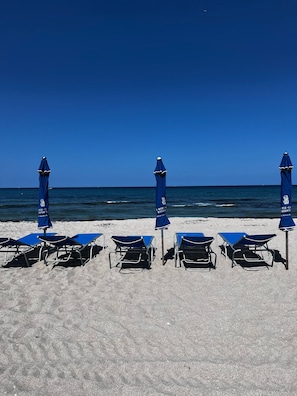 A beach with five blue sun loungers and matching umbrellas, arranged in a row on the sand. - Ritz‑Carlton Singer Island • Oceanfront Luxury 3BR 3BA Residence (Riviera Beach)