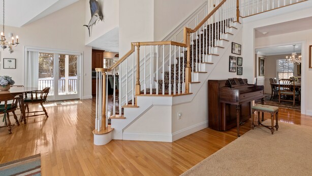 A spacious living area with a wooden staircase, a piano, and a dining area with chairs and a table. - Chatham-Walk to Town/Beach-Multi Family Friendly (Chatham)