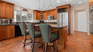 A kitchen with wooden cabinets, a stainless steel refrigerator, a microwave, and a bar area with two bar stools. - Chatham-Walk to Town/Beach-Multi Family Friendly (Chatham)