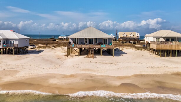 A beachfront property with multiple wooden structures, including a central building with a balcony and several smaller buildings. - Custom Beach House Steps to Beach w/ Through Lot + Panoramic Views (Dauphin Island)
