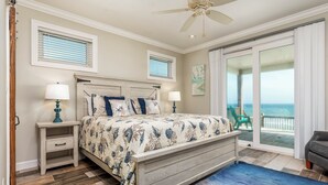 A bedroom with a bed, two bedside tables, a ceiling fan, and a view of the ocean through a sliding glass door. - Custom Beach House Steps to Beach w/ Through Lot + Panoramic Views (Dauphin Island)