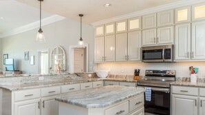 A kitchen with white cabinets, a large island with a marble countertop, a built-in microwave, and a stainless steel oven. - Custom Beach House Steps to Beach w/ Through Lot + Panoramic Views (Dauphin Island)