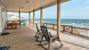 A covered deck with wooden flooring, rocking chairs, and a table with chairs. - Custom Beach House Steps to Beach w/ Through Lot + Panoramic Views (Dauphin Island)