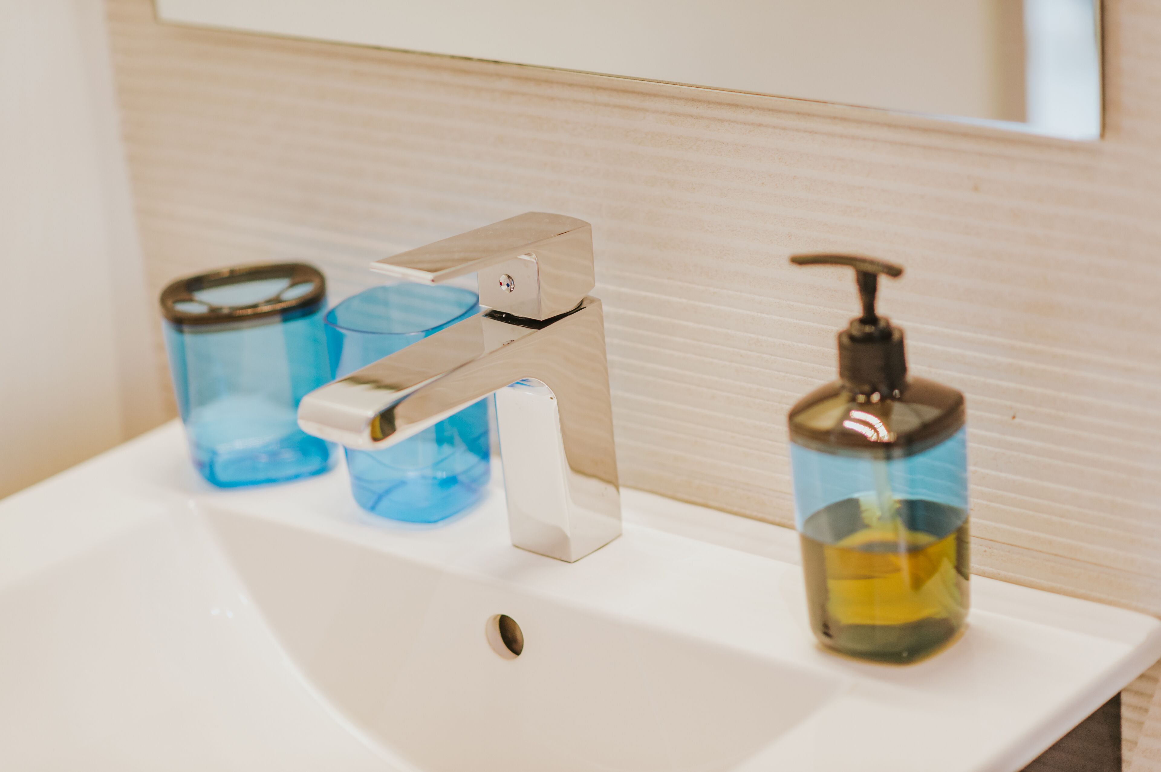 A bathroom sink with a modern faucet, two blue glass containers, and a soap dispenser.