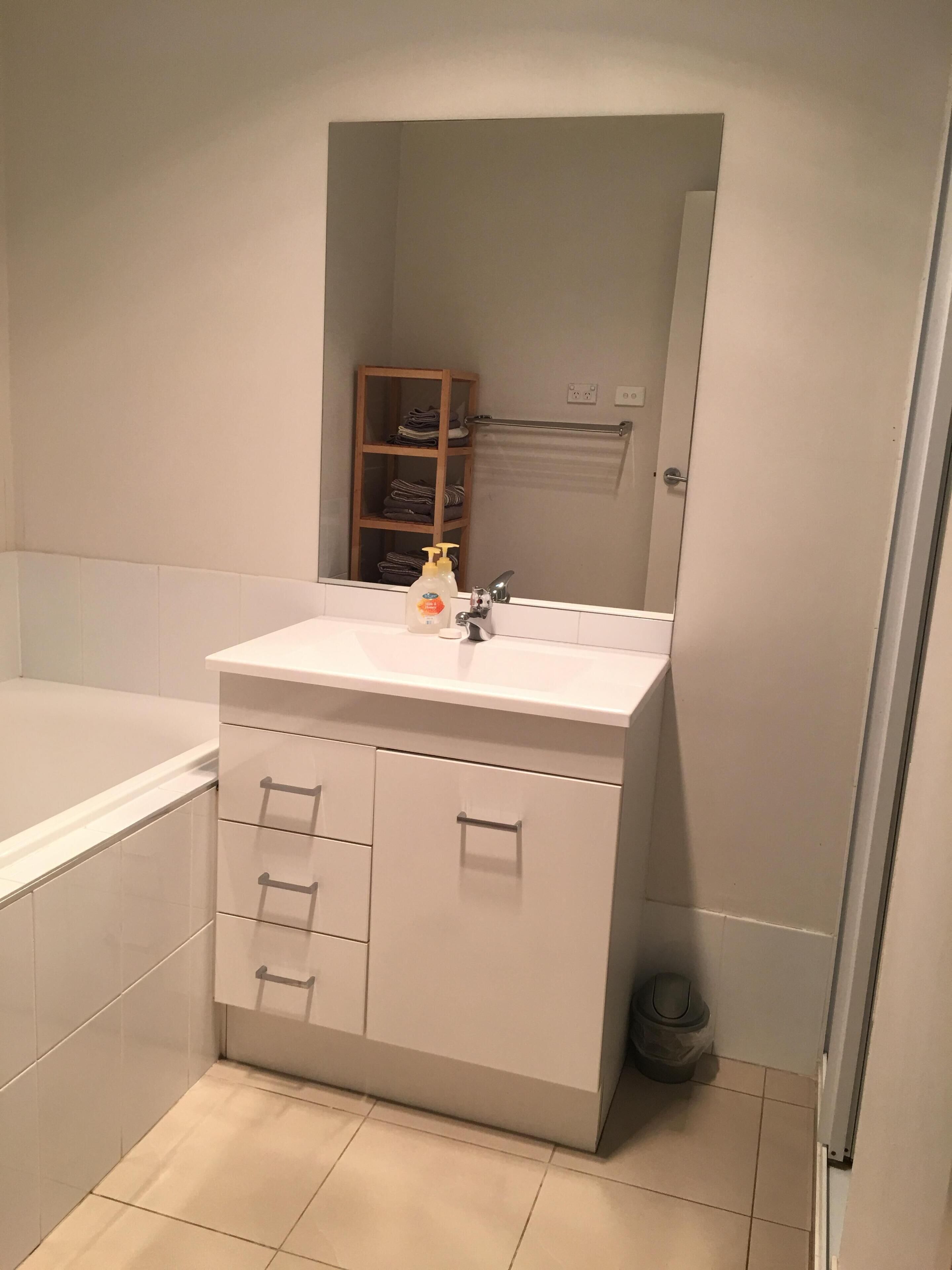 Un bany amb un lavabo blanc, un mirall, un suport per tovalloles i una petita estant amb tovalloles doblegades.