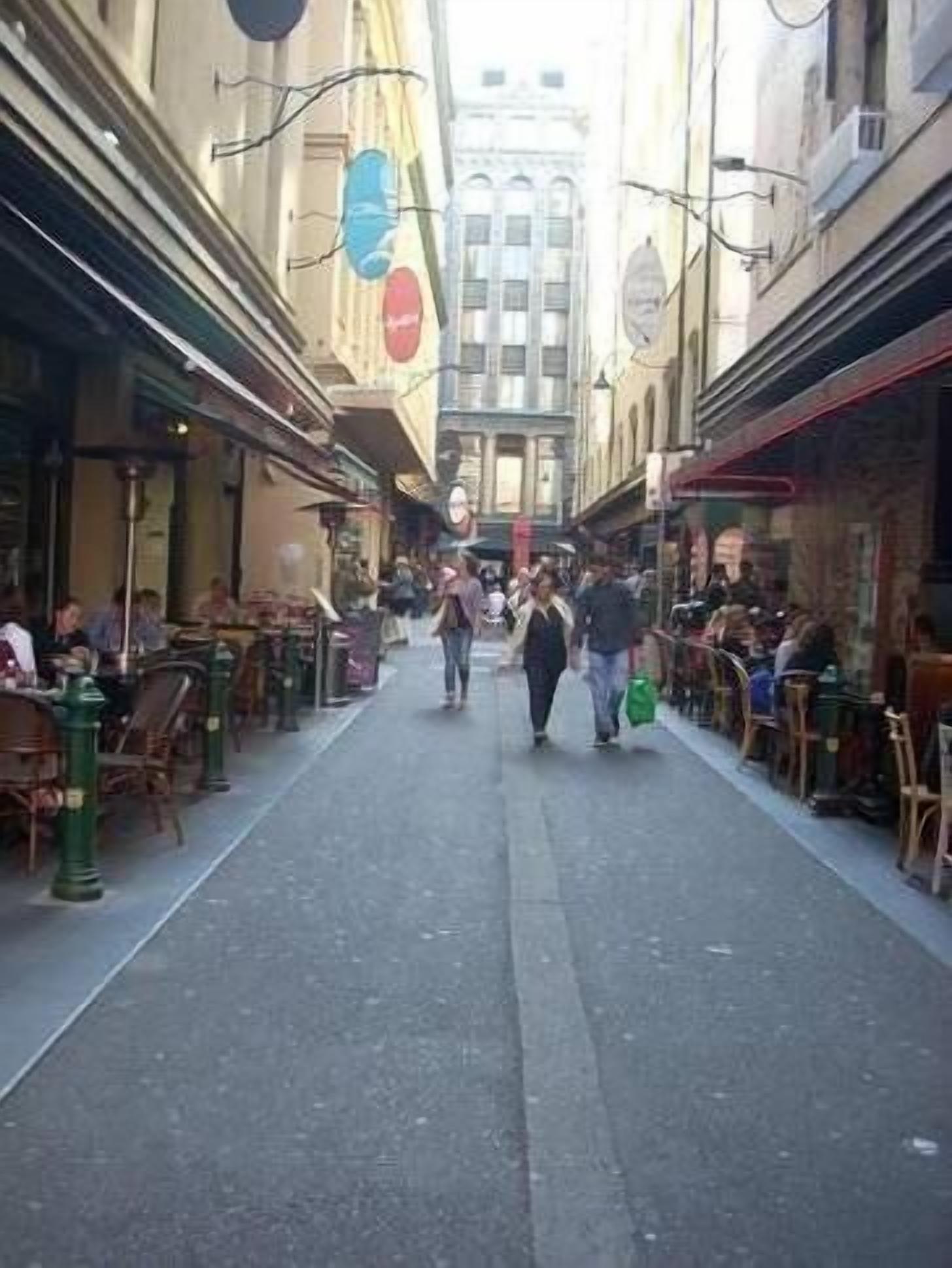 Una stretta via fiancheggiata da caffè e tavolini all'aperto, con persone che camminano e siedono.