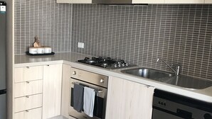 Una cuina moderna amb armaris de fusta clara, un fogó d'acer inoxidable, un forn i un rentaplats.