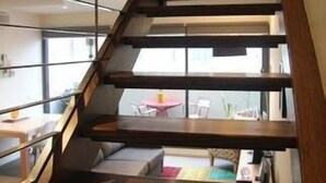 Una escala moderna amb graons de fusta i barana metàl·lica, que condueix a un nivell inferior amb una taula i cadires.