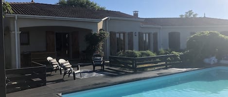 A poolside area with a clear blue pool, wooden deck, and lounge chairs.