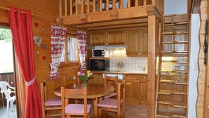 A wooden interior with a kitchen area, a dining table with chairs, and a red curtain. - Apartment in Chalet- LES HOUCHES in Résidence de Tourisme MGM (Les Houches)