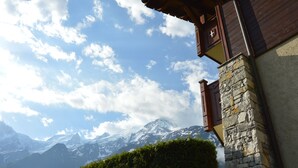 A mountain cabin with a stone facade and wooden balcony, overlooking a snow-capped mountain range. - Apartment in Chalet- LES HOUCHES in Résidence de Tourisme MGM (Les Houches)