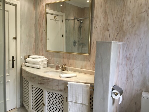 Un baño con tocador de mármol, un espejo grande, un perchero para toallas y un inodoro.