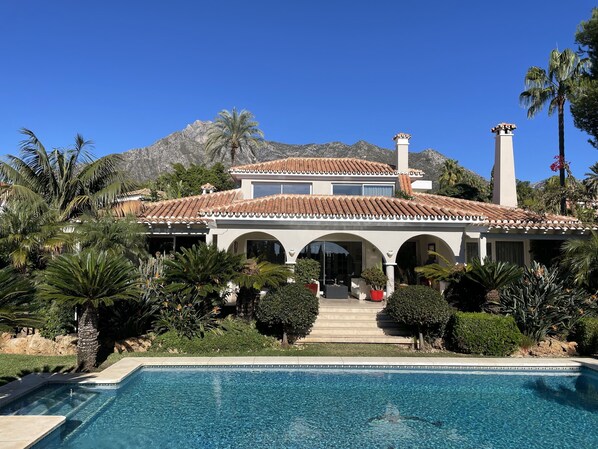 A two-story house with a swimming pool, surrounded by tropical plants and a mountain backdrop. - Luxury bright villa in Marbella Golden Mile with great sea and mountain views (marbella)