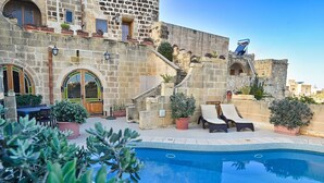 A stone building with a swimming pool, outdoor seating, and potted plants.