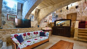A stone-walled living room with a sofa, wooden coffee table, and a television.