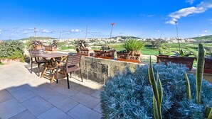 A patio with a table and chairs, potted plants, and a view of a town in the distance.