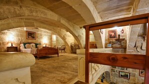 A stone-walled bedroom with a wooden bed, a nightstand, and a small table with a lamp.