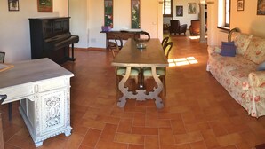 A dining area with a wooden table and chairs, a piano, and a sofa with floral upholstery. - Typical house with large pool and lovely views (Cortona)