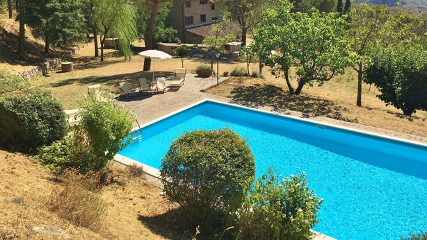 A swimming pool with lounge chairs, surrounded by trees and a stone building in a hilly landscape. - Typical house with large pool and lovely views (Cortona)