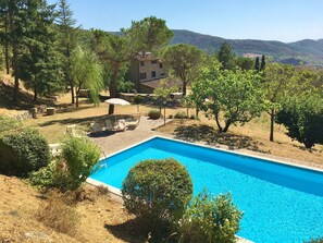 A swimming pool with lounge chairs, surrounded by trees and a stone building in a hilly landscape. - Typical house with large pool and lovely views (Cortona)