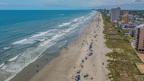 Une plage avec une longue étendue de sable, quelques parasols et des bâtiments le long du rivage.