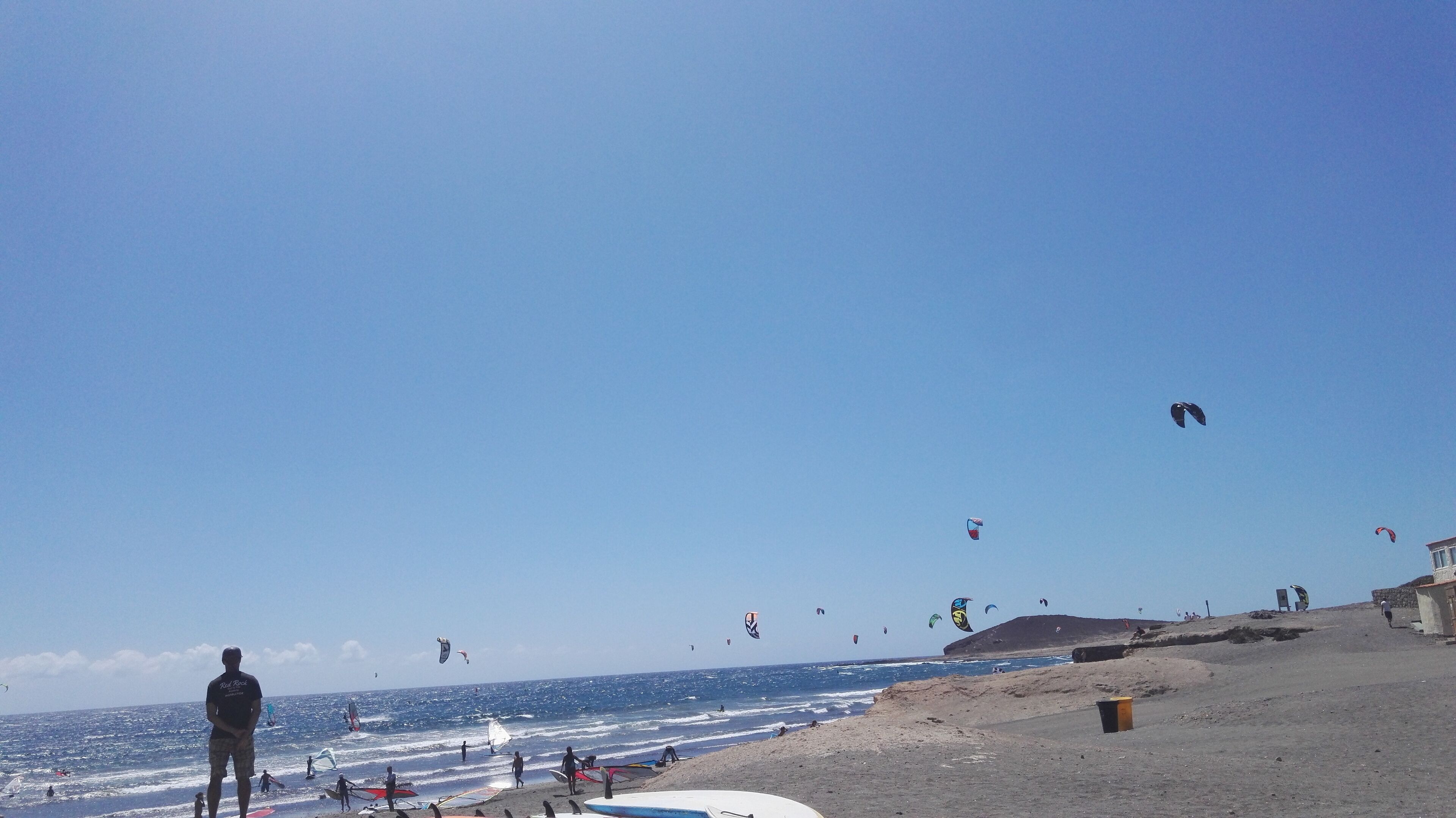 Een strand met mensen, vlieger en surfplanken.