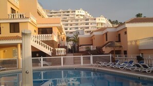 A swimming pool with a geometric tile pattern, adjacent to a building with a balcony and a staircase. - Apartment with Large Sunny Balcony with stunning views (Adeje)