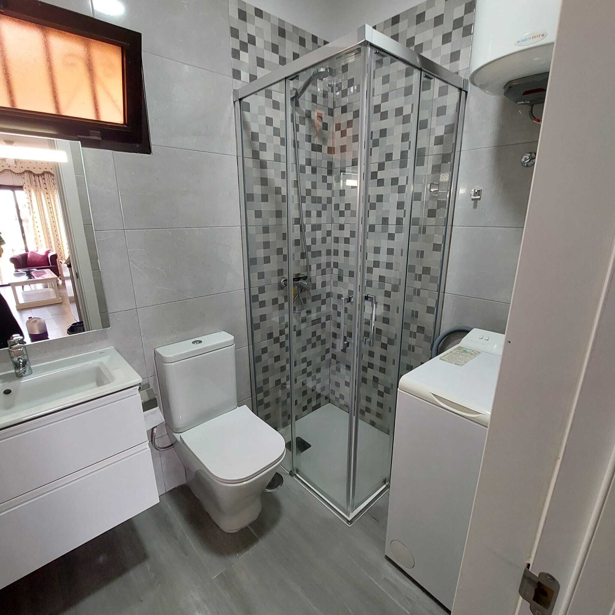 Un baño moderno con cabina de ducha de vidrio, inodoro, lavamanos y lavadora.