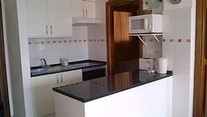 A compact kitchen with white cabinets, a black countertop, and a microwave. - Apartment with Large Sunny Balcony with stunning views (Adeje)