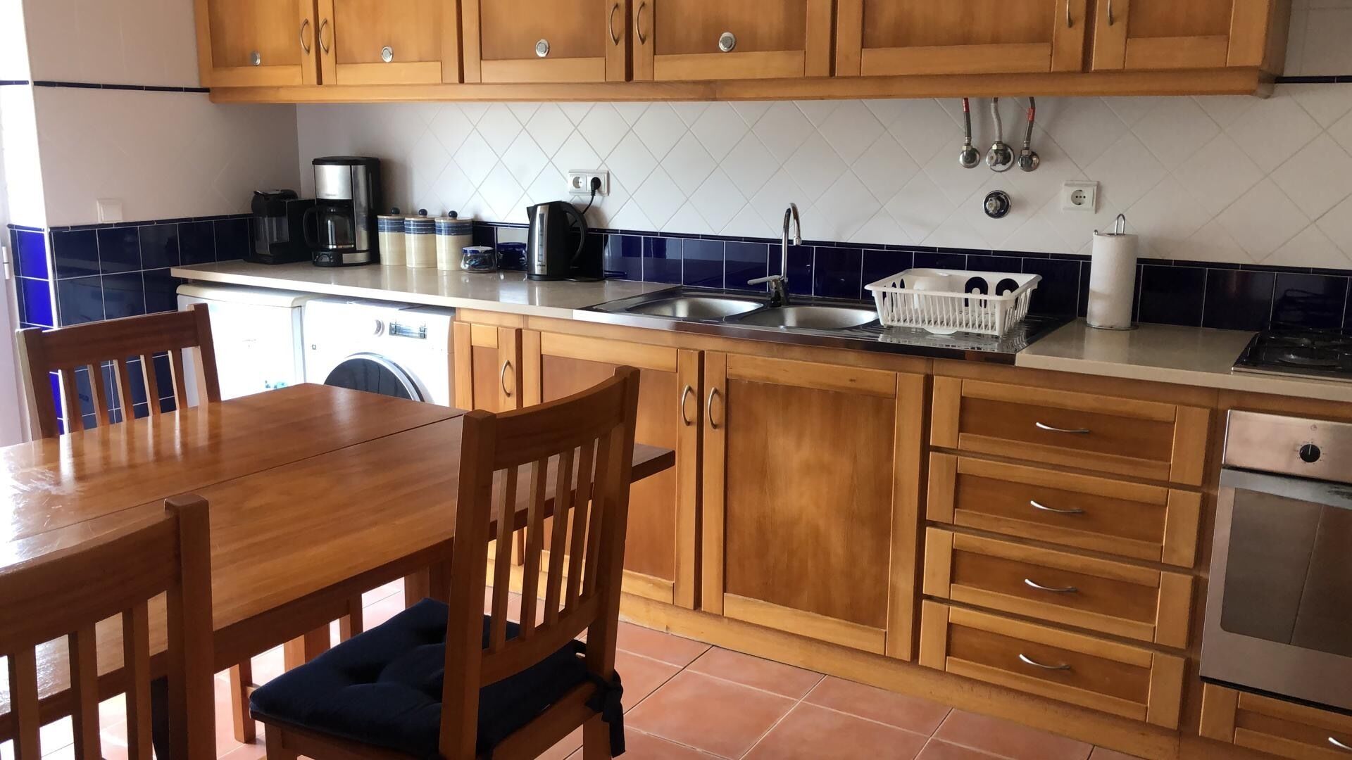 A kitchen with wooden cabinets, a dining table with chairs, a coffee maker, a sink, and a stove.