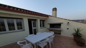 An outdoor patio with a white table and chairs, a built-in grill, and a potted plant. - La Mansarda Carbonia It (Carbonia)