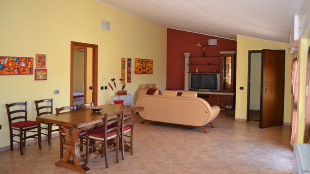 A dining area with a wooden table and chairs, a sofa, and a television in the background. - La Mansarda Carbonia It (Carbonia)
