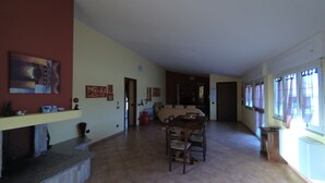 A spacious living area with a dining table and chairs, a kitchen in the background, and artwork on the walls. - La Mansarda Carbonia It (Carbonia)