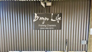 Puinen tiski, jossa on metallinen pesuallas, ja sen yläpuolella on kyltti, jossa lukee: ”Bargain Life Fishing Charters, puh. (504) 458-2876”.