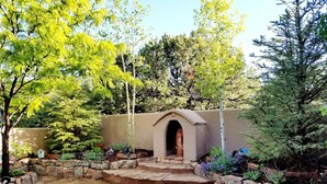 A stone courtyard with a central arched entrance, surrounded by a variety of trees and plants. - SANTA FE ADOBE JEWEL (Santa Fe)