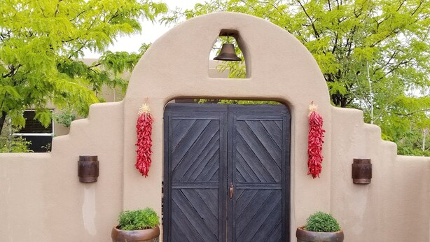 A double door with a bell above it, flanked by two potted plants and red decorations. - SANTA FE ADOBE JEWEL (Santa Fe)