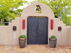 A double door with a bell above it, flanked by two potted plants and red decorations. - SANTA FE ADOBE JEWEL (Santa Fe)